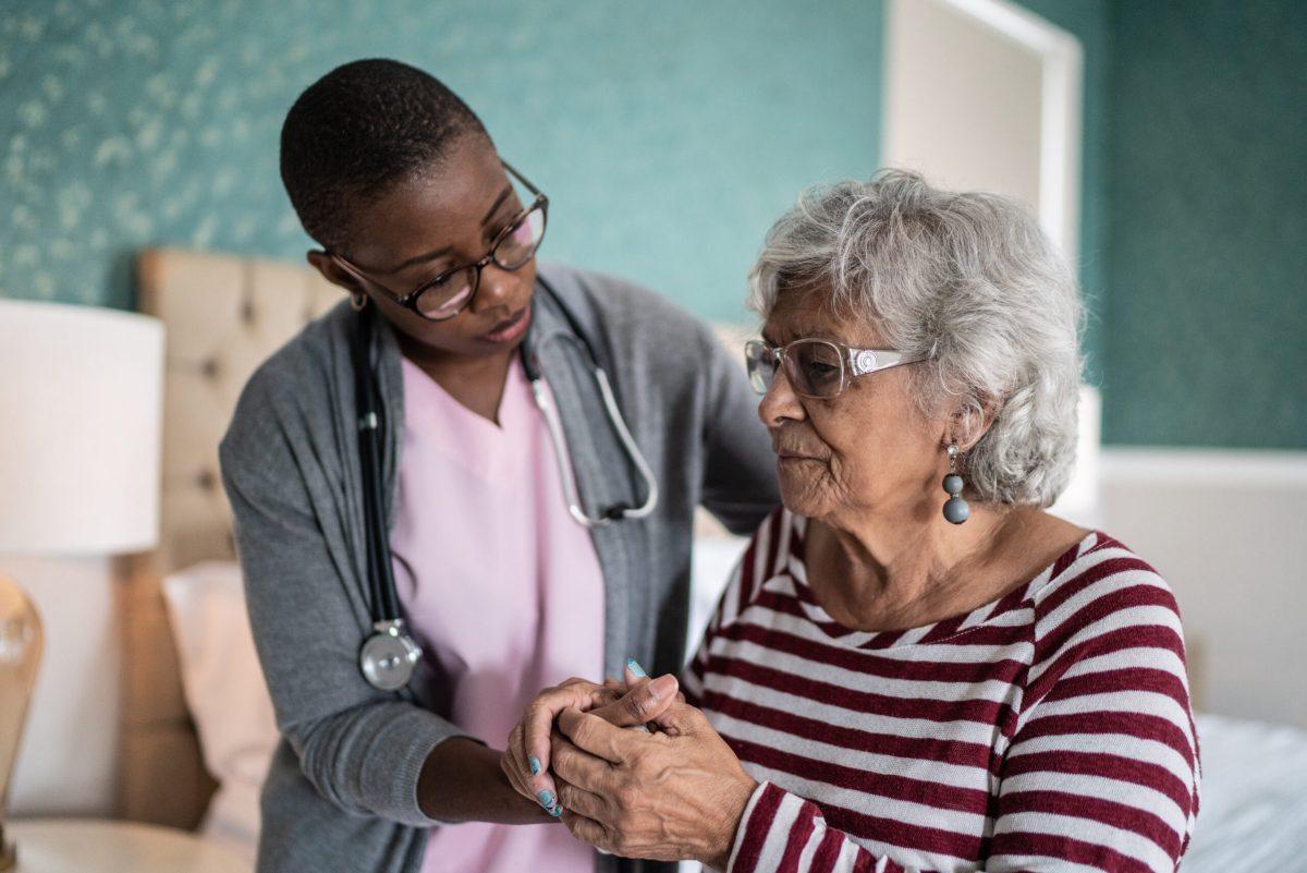 Nurse holding the hands of a patient who is sitting down.